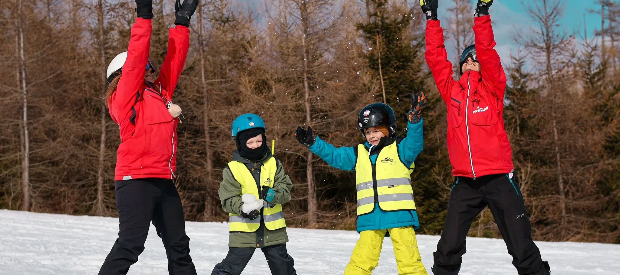 Two Premiere instructors with two children in hi-vis vests on a gentle snowy slope