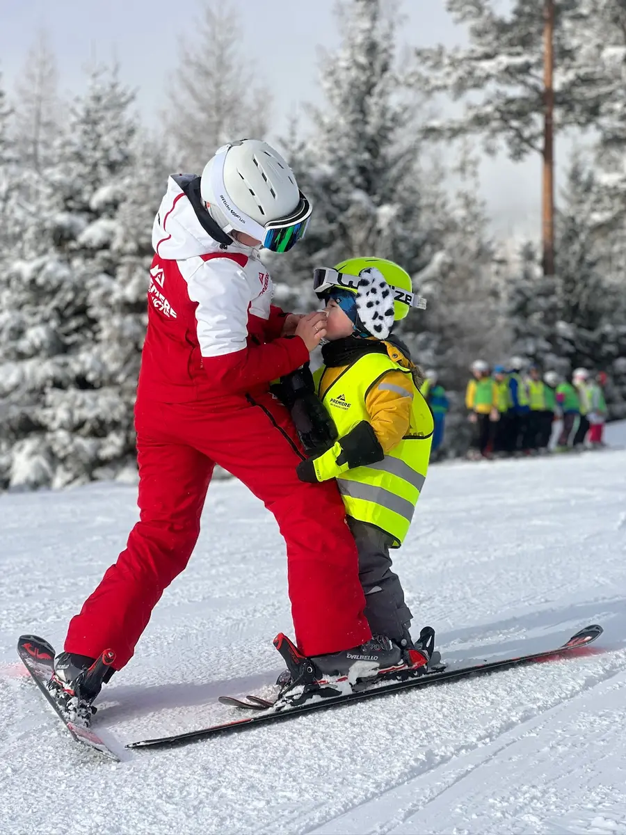 Instruktor v červené kombinéze vede dítě v reflexní vestě